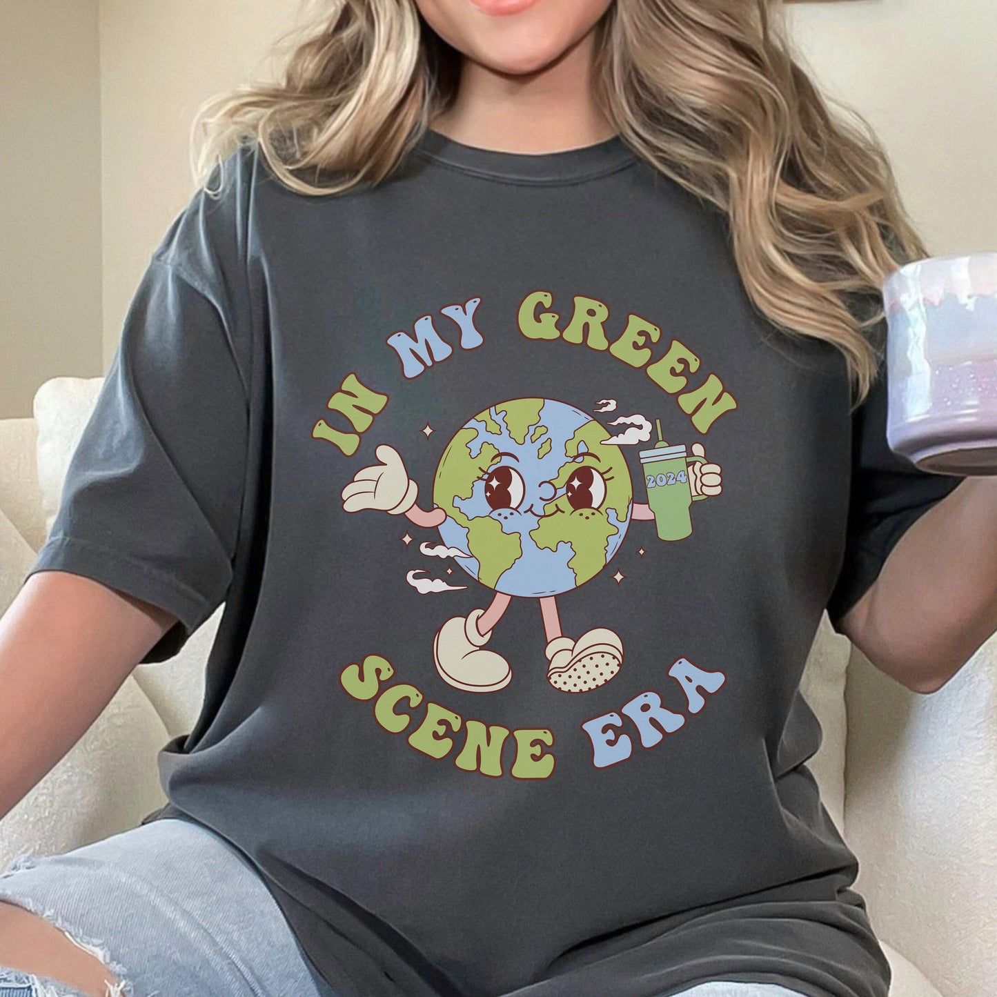 Comfort Colors Pepper Shirt with the words In my Green Scene Era with a cute earth mascot holding a tumbler with 2024 on it.